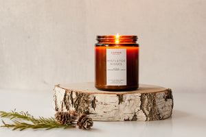 Mistletoe kisses holiday candle burning brightly in amber jar